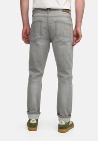 Grå denim jeans med lige pasform, der har to baglommer, subtil fading og optrukne bukseben over grønne sneakers.