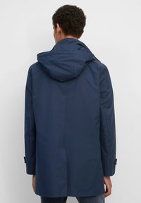 Tmavě modrý voděodolný kabát s kapucí, rovný střih a manžety s knoflíky. Hladká textura a jednoduchá silueta.