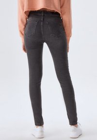 Jeans skinny en denim gris foncé avec une texture lisse, dotés de deux poches arrière et d'une taille mi-haute. Portés avec des baskets blanches.