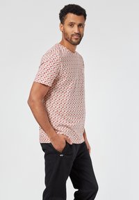 Lyhyemmillä hihoilla varustettu t-paita, jossa on punavalkoinen kukkakuosi, valmistettu kevyestä kankaasta, pyöreä kaula-aukko ja rento malli. Yhdistetty tummiin housuihin.