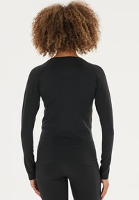 Schwarzes Langarmoberteil mit tailliertem Design, gerippten Akzenten an den Schultern, glatter Textur und rundem Ausschnitt, kombiniert mit schwarzen Leggings.