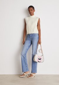 Witte mouwloze gebreide top, lichtblauwe flared jeans, beige gespsandalen met hak en een handtas met bloemenpatronen en cartoonaccenten.