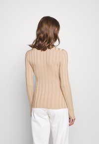 Beige ribbel trui met lange mouwen, een aansluitend ontwerp en een hoge halslijn. De stof heeft een zachte textuur met verticale strepen.
