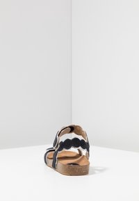 Černá plstěná sandála s ozdobnými vlnitými okraji a béžovou korkovou podrážkou. Nastavitelné pásky na suchý zip. Jednoduchý design a otevřený zadní styl.