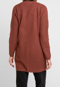 Langer, rostfarbener Strickcardigan mit strukturiertem Muster, gerippten Bündchen und abgerundetem Saum. Verfügt über lange Ärmel und eine lockere Passform.