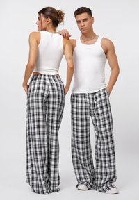 Pantaloni da pigiama a quadri bianco e nero, con una vestibilità ampia, abbinati a canotte bianche aderenti, che mostrano una texture morbida e un design casual.
