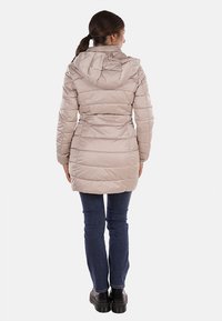 Giacca a vento beige con cappuccio, caratterizzata da un design trapuntato e maniche lunghe. Indossata sopra jeans blu e scarpe nere, vista dalla parte posteriore.