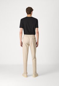 Sort kortærmet t-shirt parret med beige tætsiddende joggers, der har en elastisk talje og en baglomme. Glat stof, afslappet pasform.