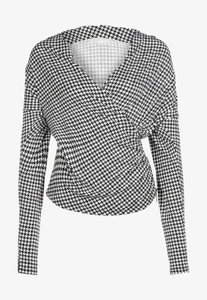Femme portant un haut pied-de-poule noir et blanc, une jupe midi plissée noire, des collants noirs et des mocassins noirs et blancs, debout.