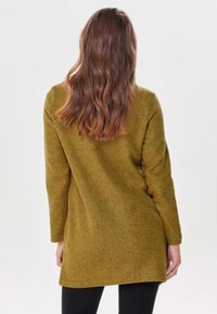 Olivgrön långärmad tunika med en avslappnad passform, strukturerad yta och en fåll som slutar vid mitten av låret, kombinerad med figurnära svarta leggings.