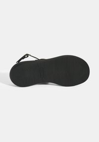 Schwarze Sandalensohle mit strukturiertem Grip-Muster und geschwungener Form. Verfügt über ein kleines Logo und einen Riemenanschluss für eine verstellbare Passform.