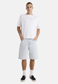 White short-sleeve t-shirt, light blue denim shorts, black slip-on shoes, white crew socks. Minimalist design with no visible patterns.