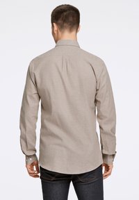 Camicia a maniche lunghe color marrone chiaro con una texture sottile, polsini abbottonati e colletto classico, indossata con jeans in denim scuro.