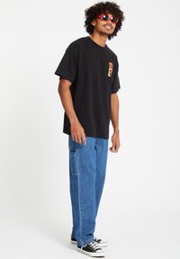 Black cotton t-shirt with a small graphic on the chest, paired with light blue denim cargo pants and black sneakers. Red sunglasses complete the look.