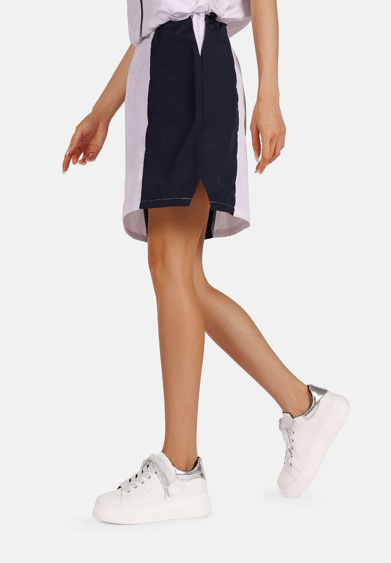 Gonna a blocchi di colore bianco e navy con vita regolabile, caratterizzata da uno spacco laterale. Abbinata a sneakers bianche con dettagli argentati.