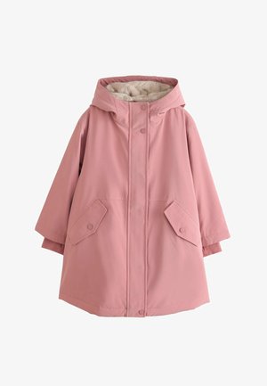 Person iført en pink jakke med guld trykknapper og lynlås, der viser en hånd delvist inde i ærmet med en matchende pink manchet.