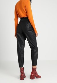 Černé kožené kalhoty s užším střihem, s vysokým pasem. Kombinované s červenými kotníkovými botami s hadím vzorem a oranžovým svetr.