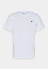 T-shirt blanc uni à manches courtes avec col rond et petit logo crocodile vert Lacoste sur la poitrine gauche.