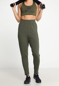 Oliveově zelená sportovní podprsenka Nike a odpovídající tepláky z měkké, elastické látky, s elastickým pasem a stahovacími ankly, doplněné černými teniskami.