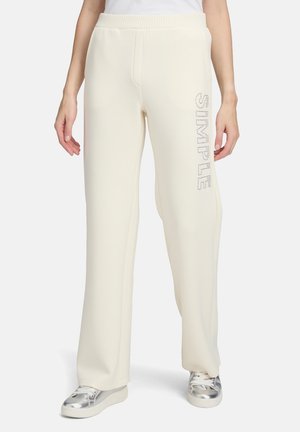 Pantalons de survêtement couleur crème avec une coupe décontractée, présentant une taille côtelée et le mot "SIMPLE" en strass le long de la jambe gauche.
