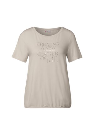 Camiseta de manga corta beige con cuello redondo, que presenta el texto metálico "CREANDO UN NUEVO CAPÍTULO DE MÍ" en el frente.