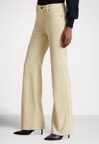 Beżowe rozszerzane dżinsy z miękkiej mieszanki bawełny, z pasem z szlufkami na pasek i detalami przednich kieszeni. W połączeniu z czarnymi butami na obcasie o szpiczastym nosku.