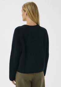 Ciemny granatowy sweter z prążkowanej dzianiny, okrągłym dekoltem i długimi rękawami, charakteryzujący się luźnym krojem i miękką teksturą.