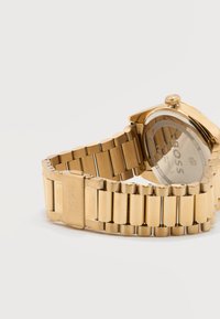 Χρυσό μεταλλικό ρολόι χειρός με συνδεδεμένο μπρασελέ και χαραγμένο κλείσιμο, που δείχνει την πίσω θήκη με την ένδειξη "BOSS" και λεπτομέρειες αντοχής στο νερό.