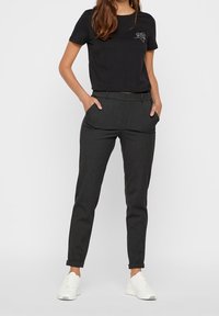 Černé tričko s krátkým rukávem a potiskem na přední straně, kombinované s elegantními tmavě šedými kalhotami s předními kapsami a slim fit. Bílé tenisky.