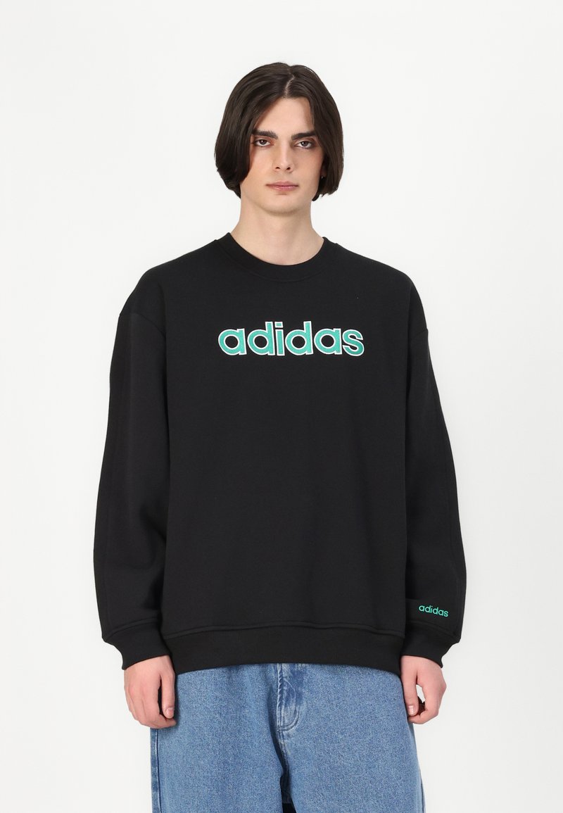 Sweatshirt preto feito de algodão com gola redonda, apresentando um ousado logótipo "adidas" em verde na parte frontal e um logótipo adicional na manga.