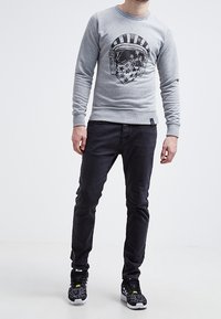 Sudadera gris con estampado gráfico de un casco y estrellas, combinada con pantalones negros ajustados y zapatillas negras con acentos en blanco y amarillo.