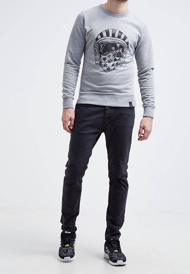 Sudadera gris con estampado gráfico de un casco y estrellas, combinada con pantalones negros ajustados y zapatillas negras con acentos en blanco y amarillo.