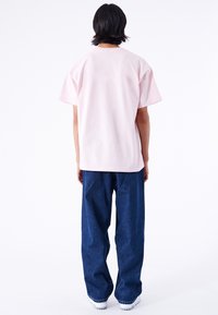 Camiseta de algodón rosa claro con mangas cortas, cuello redondo y detalle de costura en la parte posterior, combinada con pantalones de mezclilla oscuros y holgados.