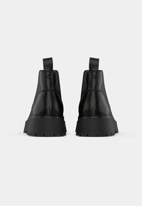 Čierne kožené členkové topánky s hladkým povrchom, zdvihnutou hrubou podrážkou a dvojitými pútkami vzadu pre ľahké obúvanie.
