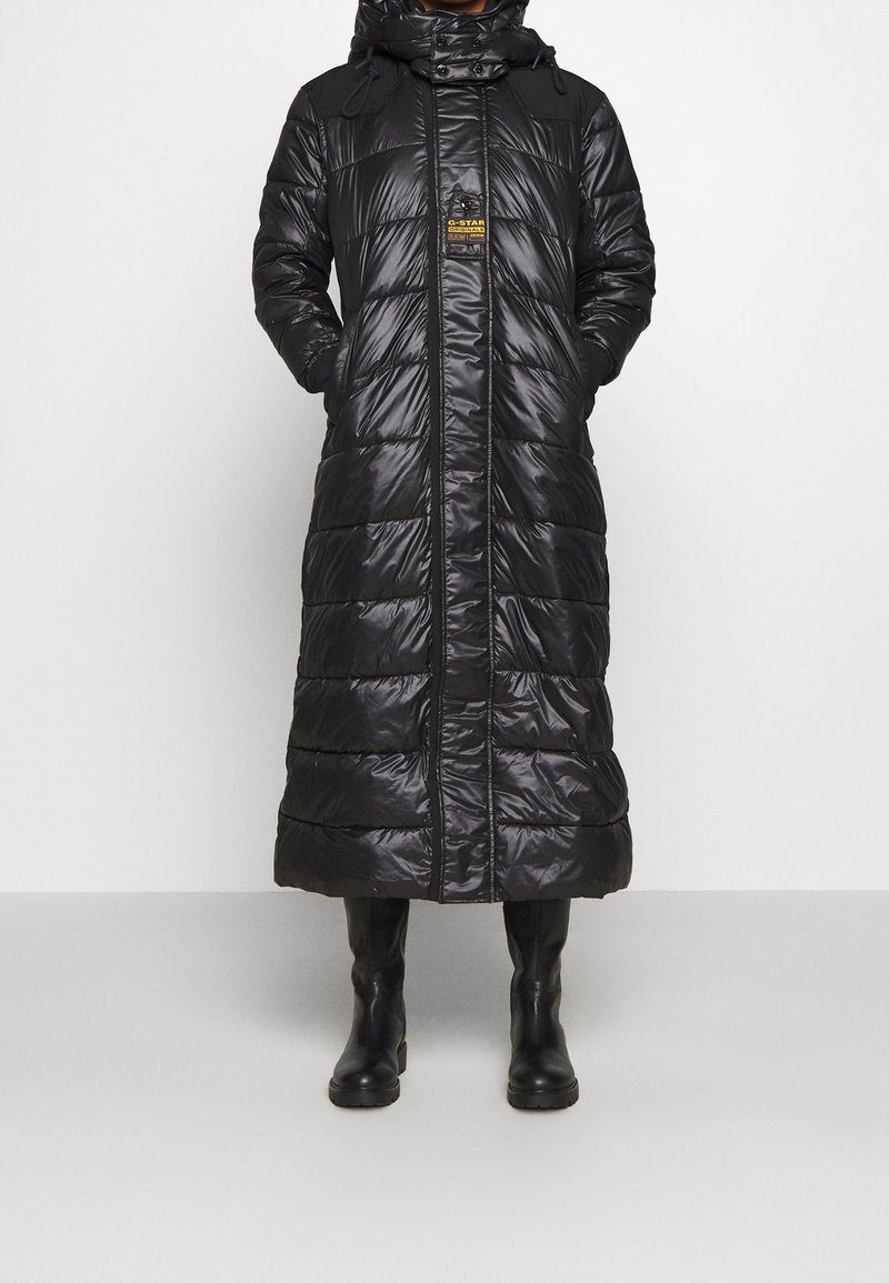 Abrigo tipo puff negro con diseño largo, cuenta con capucha, textura brillante, patrón de acolchado horizontal y cierre delantero de cremallera.