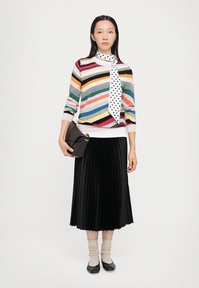 Maglione a righe multicolore in maglia, abbinato a una sciarpa bianca a pois, con una gonna plissettata nera e calze beige, mentre tiene una pochette nera.