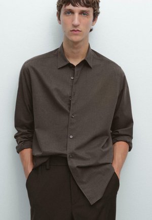 Brown long-sleeve button-up shirt with a soft texture, featuring a collar, single pocket, and rolled cuffs, paired with dark trousers.