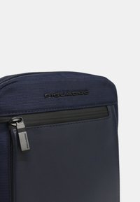 Borsa Piquadro blu navy con tessuto testurizzato e accenti in pelle liscia. Chiusura con zip e una elegante linguetta in metallo.