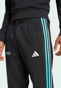 Black joggers with turquoise stripes down the sides, elastic waistband with drawstring, featuring white Adidas logo and AMG Petronas branding.