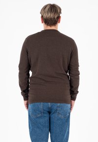 Maglione marrone a maniche lunghe con polsini e orlo a coste, texture liscia, abbinato a jeans in denim blu chiaro. Vista da dietro.