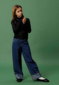 Must nagu zip-up jakk pika varrukaga, koos vabade siniste teksadega, millel on voltitud hem. Mustad balletisandaalid valgete sokkidega.