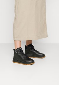 Schwarze High-Top-Sneaker aus Leder mit strukturierten Einsätzen, ausgestattet mit einer Gummilaufsohle und einem Schnürdesign für festen Halt.