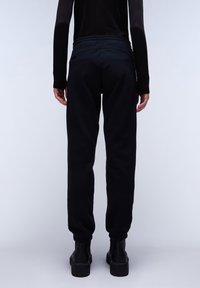 Schwarze Jogginghose mit einem Kordelzugbund, tapered Beinen und gerippten Bündchen, aus weichem Stoff. Tragend mit schwarzen Plateaustiefeln.