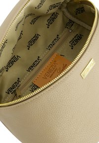 Lys beige l�ædertaske indvendig med en lynlåslomme og et mærke med teksten "VENEZIA". Foret med mønstret stof i dæmpede nuancer.