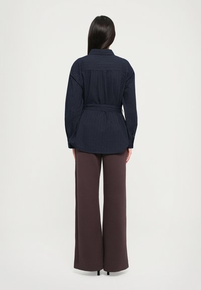 Navy striped blouse with a belted waist, featuring a collar and button closure. Paired with wide-leg brown trousers.