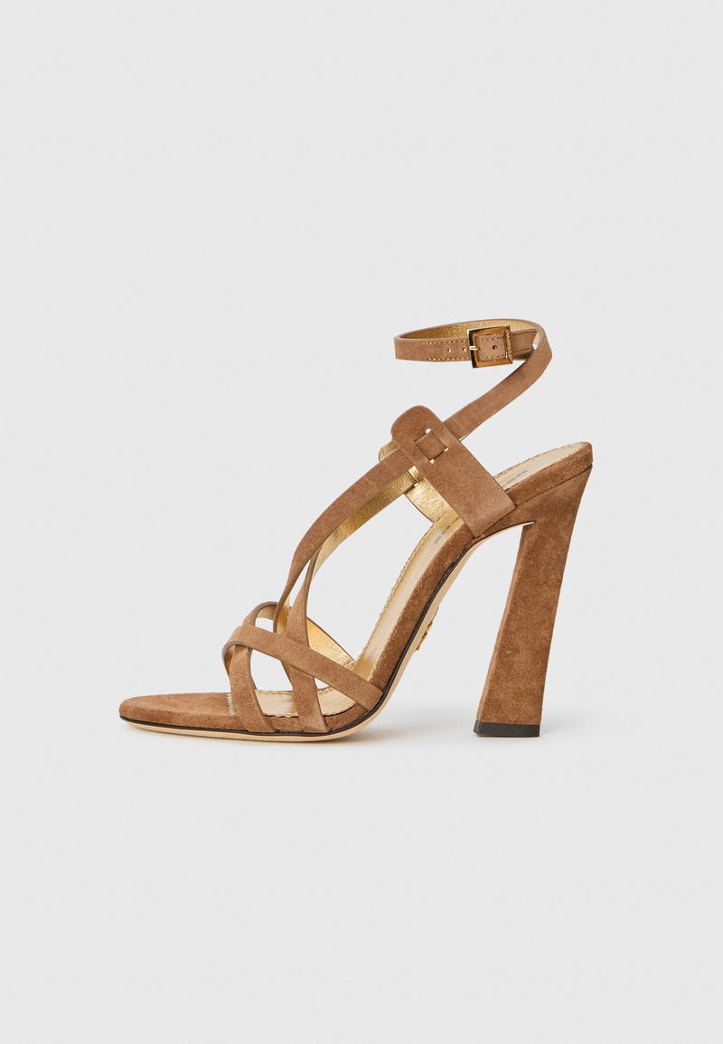 Suede high-heeled sandal in tan with cross-straps and ankle strap. Features a gold-tone accent and a chunky, textured heel.