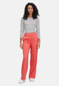 Coral wide-leg trousers with an elastic waistband, paired with a black-and-white striped long-sleeve shirt and white sneakers.