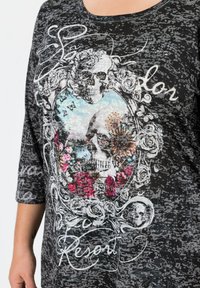 Schwarzes grafisches T-Shirt mit einem zentralen Design aus Schädeln, Blumen und Schmetterlingen, verziert mit Pailletten und filigranen Mustern.