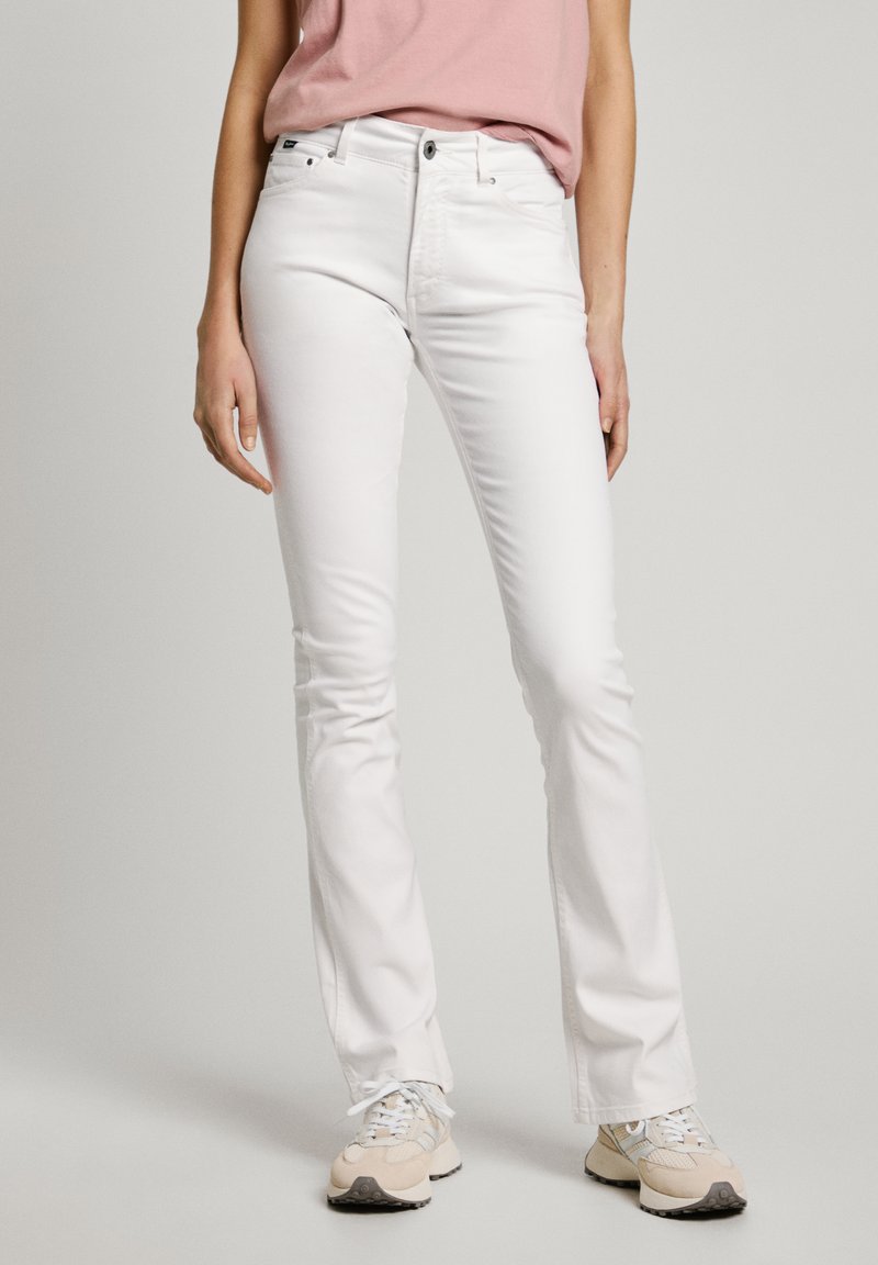 Jeans blancos acampanados con una textura suave, presentan un cierre de cremallera, cinco bolsillos y un corte clásico. Se llevan con zapatillas de colores claros.