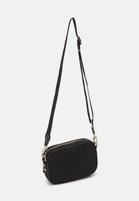 Bolso bandolera de tela negra con forma rectangular, cierre de cremallera y correa ajustable. Cuenta con herrajes en tono dorado y una textura suave.